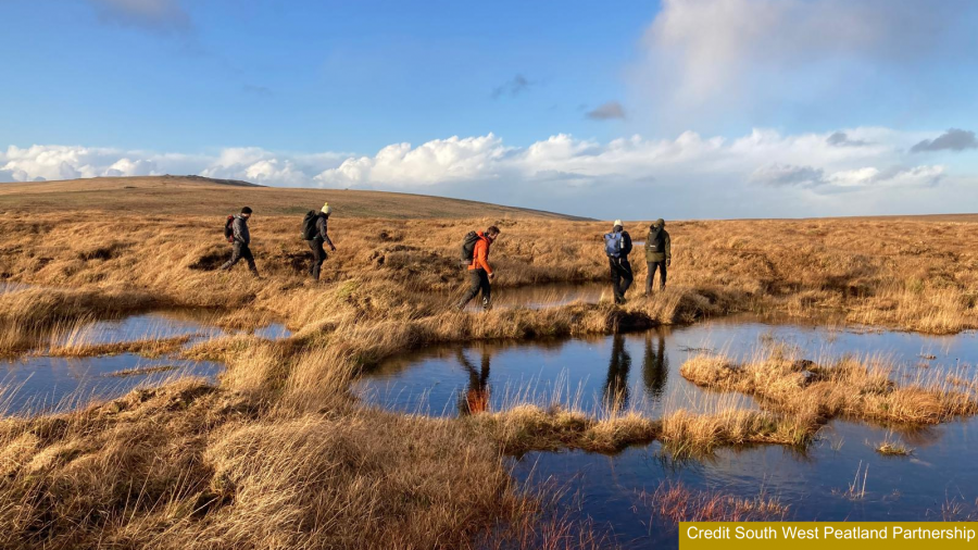 People in outdoor clothing walking across a landscape of bog pools