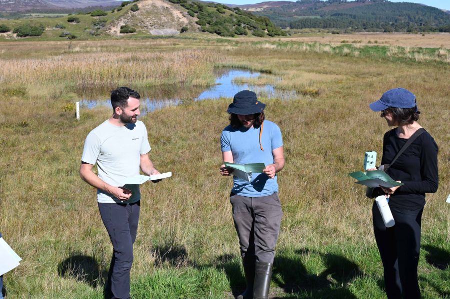 People standing on a bog in the sunshire reading from notes