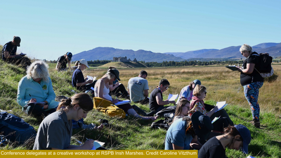 Conference delegates at RSPB Insh Marshes writing letters to school children with Ruthven Barracks in the background.