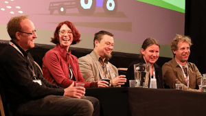 Group of smiling people sat at a table with a graphic of a tractor on a screen behind them.