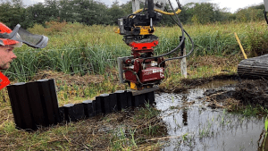 Plastic dam being installed in a reed bed by a large hydraulic machine arm