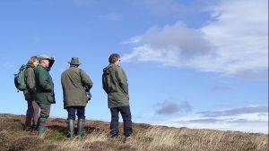 Four people in outdoor clothing looking out across a peatland landscape. Image credit: Mark Reed