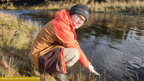 Young man in outdoor clothing crouched next to a river